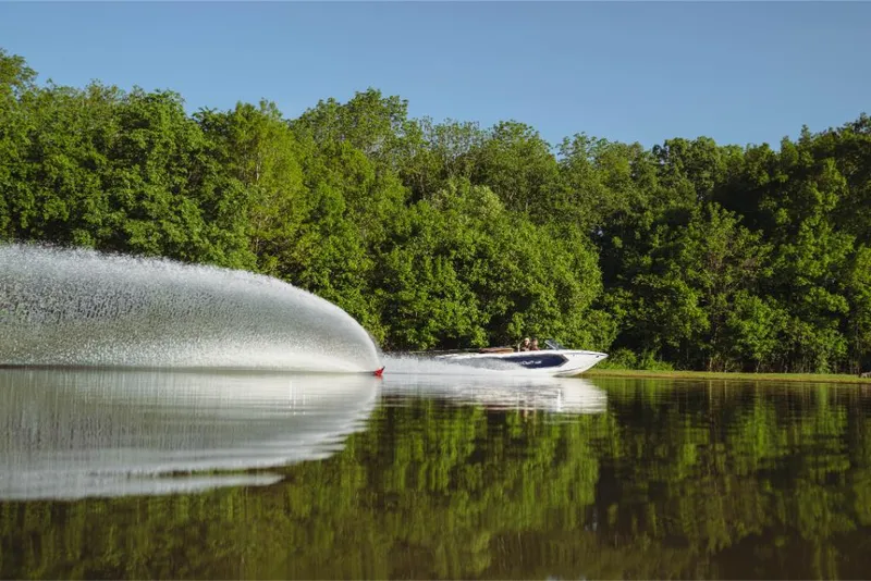 Slide: The Image of 2023 MasterCraft ProStar boat on a serene lake with lush green trees. - 7
