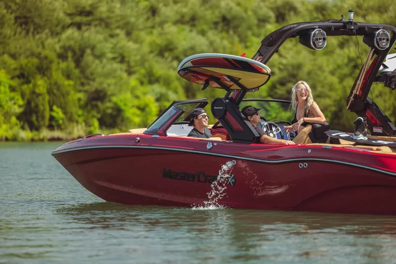 Slide: The Image of 2023 MasterCraft X24 boat cruising on a lake with passengers enjoying the ride. - 0