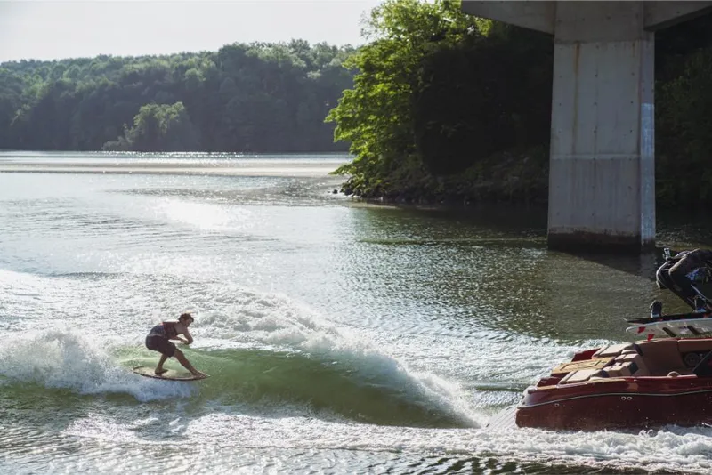 Slide: The Image of 2023 MasterCraft X24 boat creating waves for a wakeboarder on a scenic lake. - 14