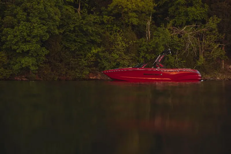 Slide: The Image of 2023 MasterCraft X24 boat on a calm lake near a forested shoreline. - 16