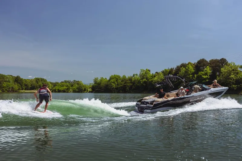 Slide: The Image of 2023 MasterCraft X26 boat towing a wakeboarder on a sunny lake. - 1