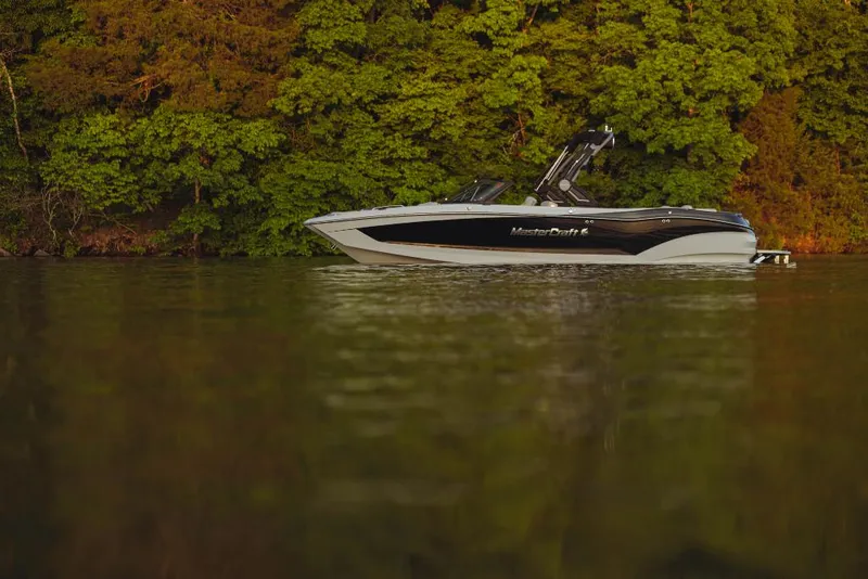 Slide: The Image of 2023 MasterCraft X26 boat on calm water with lush green forest background. - 16