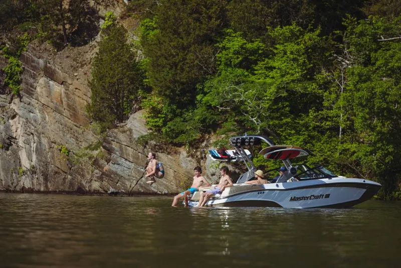 Slide: The Image of People enjoying a day on a 2023 MasterCraft XT20 boat near a rocky shoreline. - 1