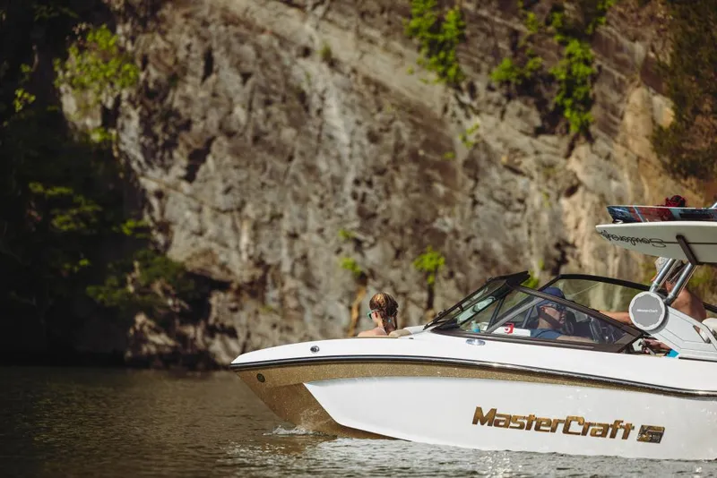 Slide: The Image of 2023 MasterCraft XT20 boat cruising near rocky cliffs. - 2