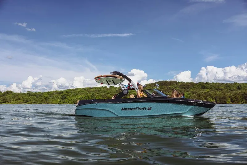 Slide: The Image of 2023 MasterCraft XT22 boat on a lake with lush green shoreline. - 1