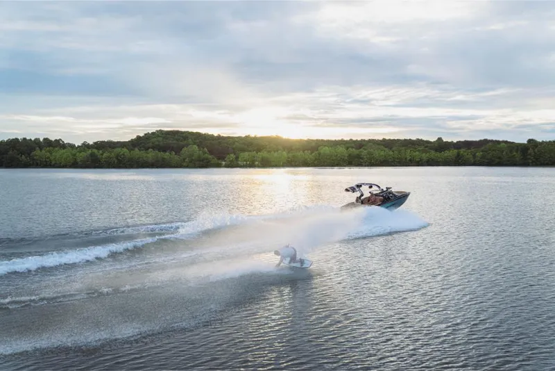 Slide: The Image of 2023 MasterCraft XT22 boat towing a wakeboarder on a serene lake at sunset. - 12