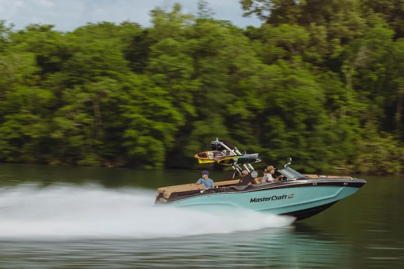 Slide: The Image of 2023 MasterCraft XT22 speedboat cruising on a lake with lush green trees in the background. - 14