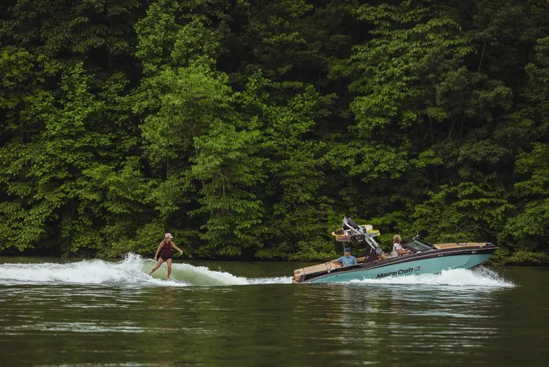 Slide: The Image of 2023 MasterCraft XT22 towing a wakeboarder on a lake with lush green trees in the background. - 16