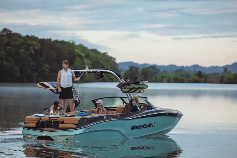 Slide: The Image of 2023 MasterCraft XT22 boat on a serene lake with people enjoying water activities. - 18