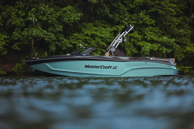 Slide: The Image of 2023 MasterCraft XT22 boat on a lake with lush green trees in the background. - 2