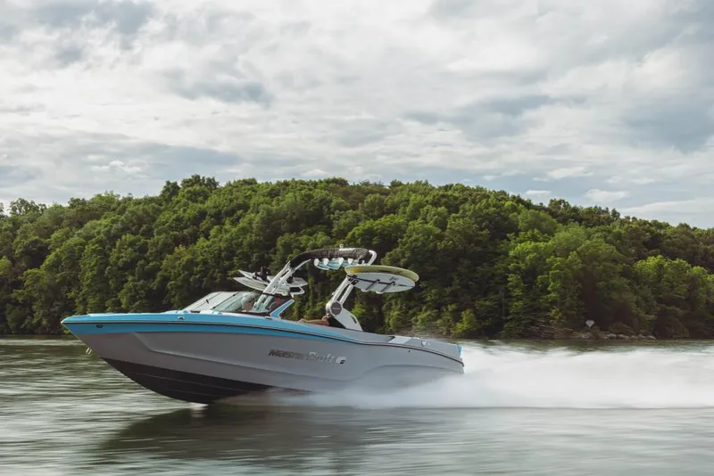 Slide: The Image of 2023 MasterCraft XT23 boat speeding on a lake with lush green trees in the background. - 8