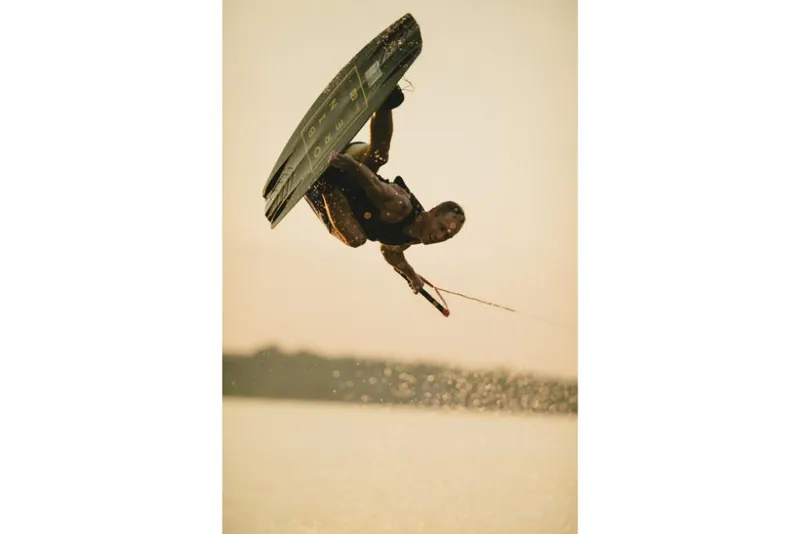 Slide: The Image of Wakeboarder performing a trick behind a 2022 MasterCraft XT25 boat at sunset. - 11