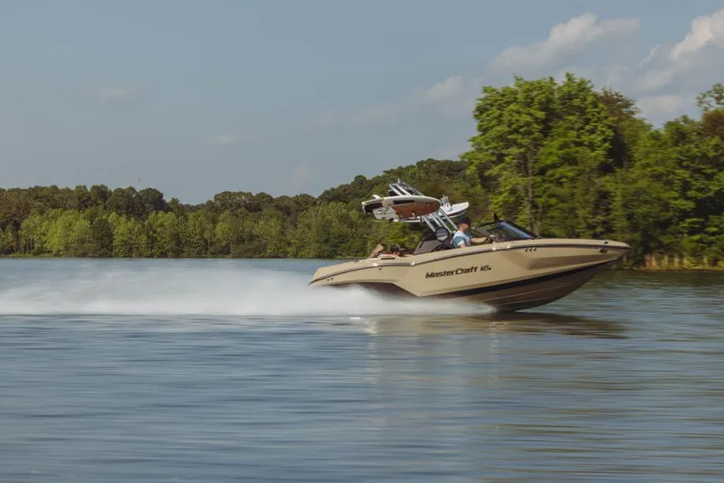 Slide: The Image of 2023 MasterCraft NXT20 speeding on a lake with lush green trees in the background. - 13