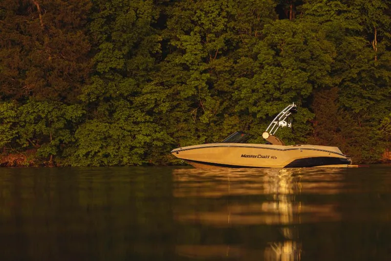 Slide: The Image of 2023 MasterCraft NXT20 boat on a calm lake with a forested background. - 15