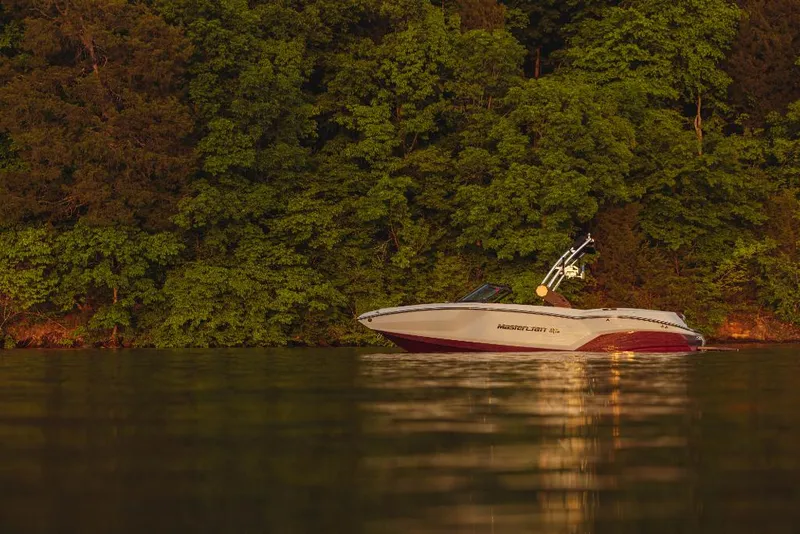 Slide: The Image of 2023 MasterCraft NXT22 boat on a calm lake near a forested shoreline. - 13
