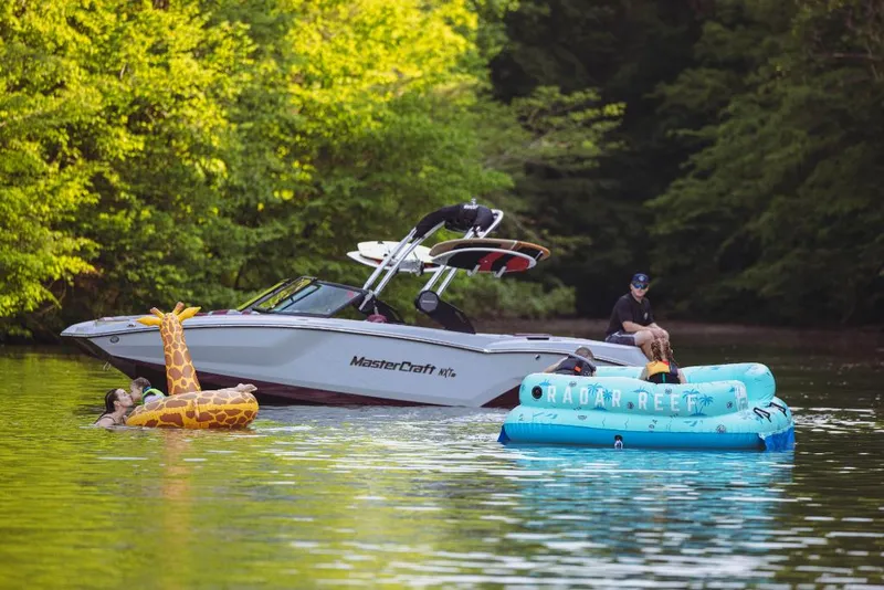 Slide: The Image of 2023 MasterCraft NXT22 boat on a lake with people enjoying inflatables. - 4