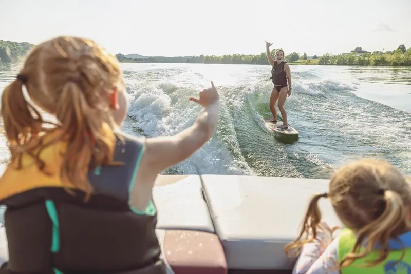 Slide: The Image of 2023 MasterCraft NXT22 boat with kids watching a woman wakesurfing on a lake. - 7