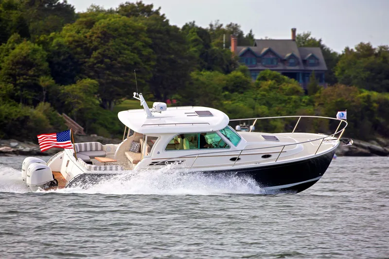 The Image of 2024 Back Cove 34O cruising on water near a forested shoreline. - 0