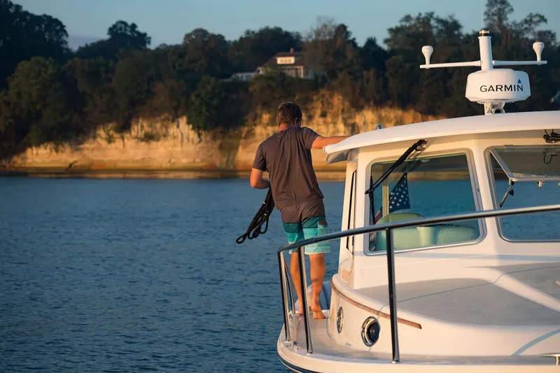 Slide: The Image of Man on 2024 Back Cove 34O boat at sunset, holding rope, near scenic shoreline. - 15