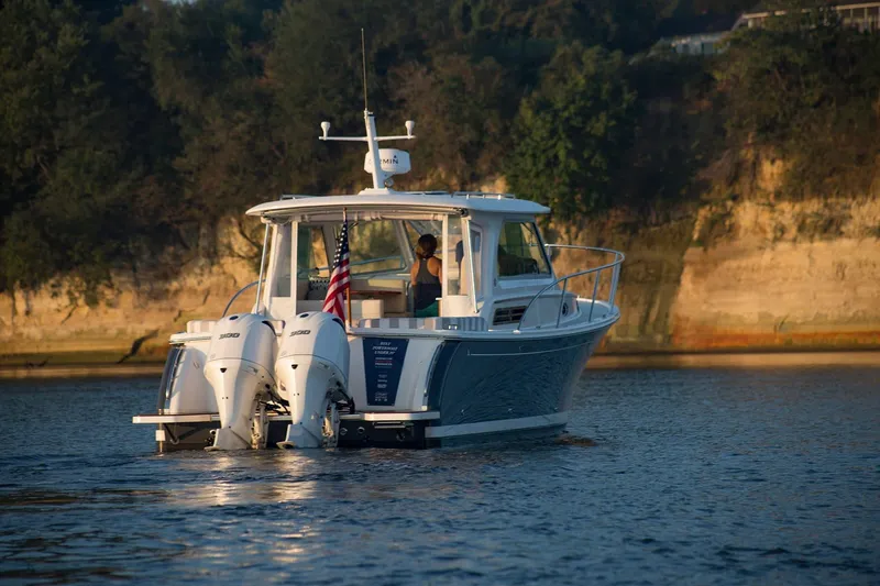 Slide: The Image of 2024 Back Cove 34O boat cruising on a lake with scenic cliffs in the background. - 7