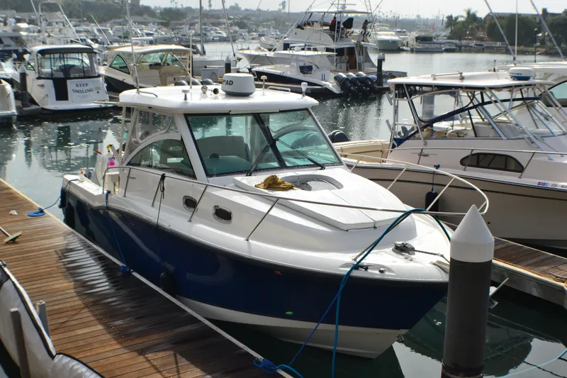 Slide: The Image of 2016 Boston Whaler 315 Conquest boat with blue hull, docked under clear sky. - 2