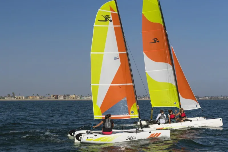 Slide: The Image of 2023 Hobie Cat Wave sailboats on the water with colorful sails. - 4