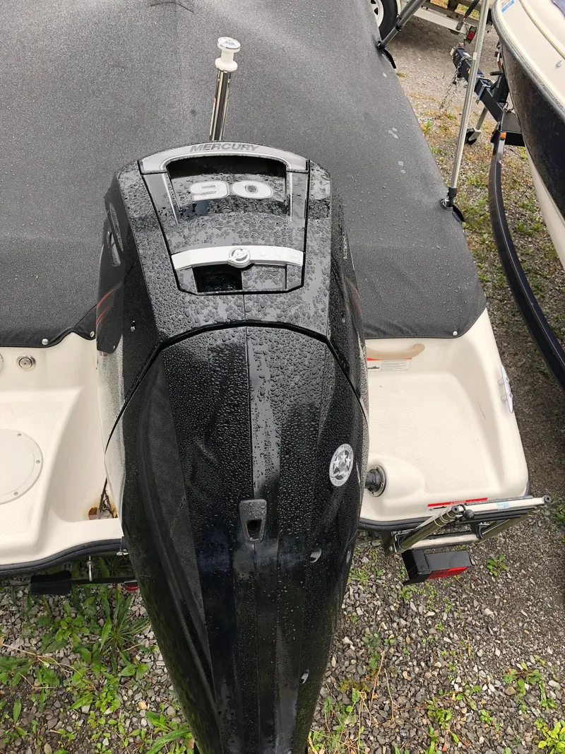 Slide: The Image of 2018 Bayliner 160 Bowrider with covered outboard motor, parked on gravel. - 2
