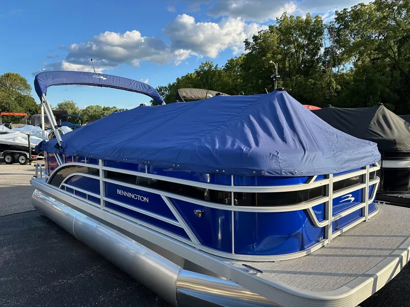 Slide: The Image of 2025 Bennington 21 SSR Quad Bench pontoon boat with blue cover, parked outdoors. - 15