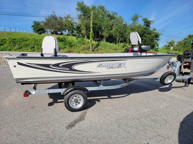 The Image of 2025 Smoker Craft 16' Angler Patriot Tiller fishing boat on trailer, parked outdoors. - 1