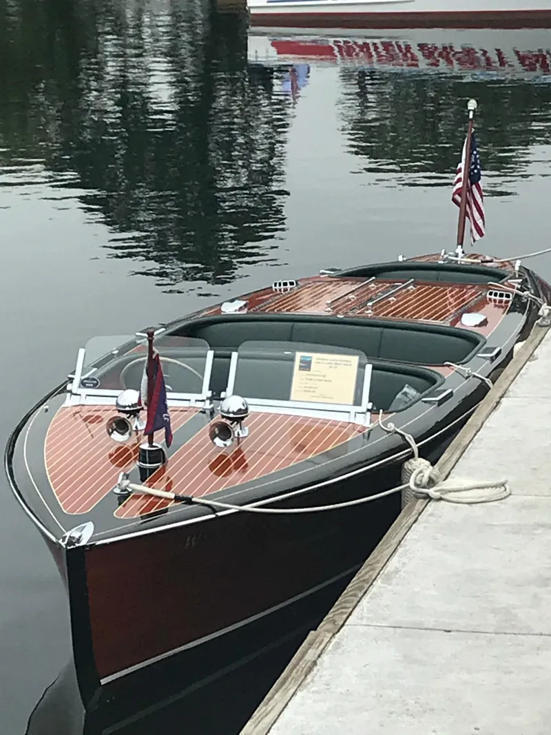 Slide: The Image of 1940 Chris-Craft Deluxe Runabout boat docked on calm water with American flag. - 6