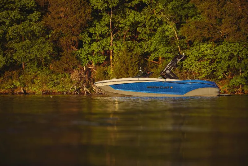 Slide: The Image of 2023 MasterCraft X22 boat on a calm lake near a forested shoreline. - 17