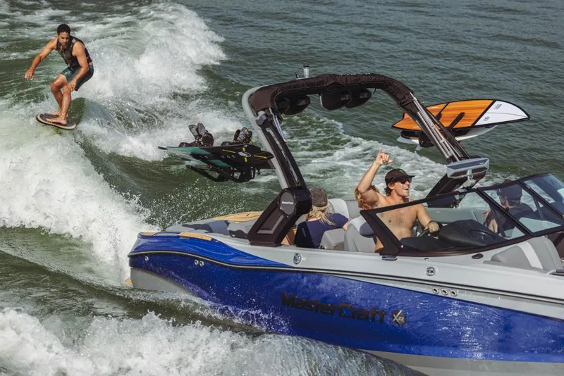 Slide: The Image of 2023 MasterCraft X22 boat towing a wakeboarder on a lake. - 2