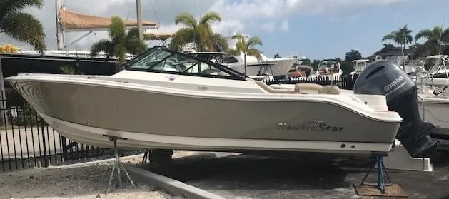 Slide: The Image of 2019 NauticStar 2302 LDC boat on display, surrounded by palm trees and other boats. - 0