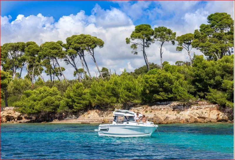 Slide: The Image of 2024 Jeanneau NC 795 boat cruising near a lush, tree-lined shoreline. - 10