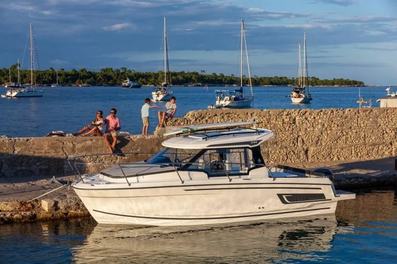Slide: The Image of 2024 Jeanneau NC 795 boat docked by a stone pier with people relaxing nearby. - 30