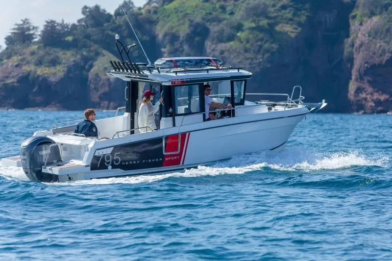 Slide: The Image of 2023 Jeanneau NC795 Sport Series 2 boat on calm water with two people on rocky shore. - 19