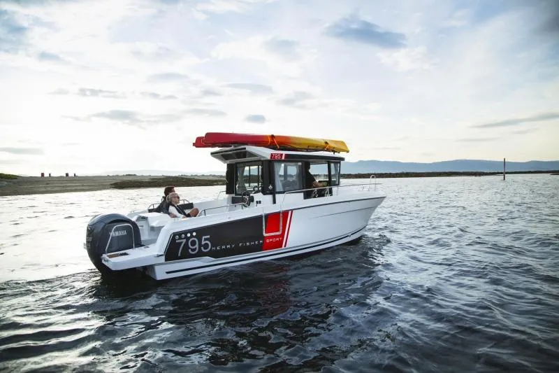 Slide: The Image of 2023 Jeanneau NC795 Sport Series 2 boat on calm water with two people on rocky shore. - 20