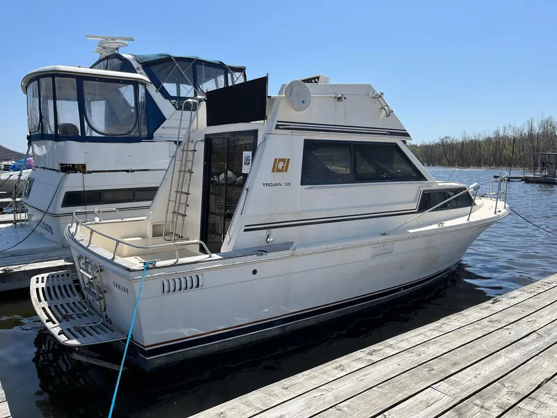 Slide: The Image of 1980 Trojan F-30 Flybridge Sedan docked at marina, clear sky, calm water. - 0