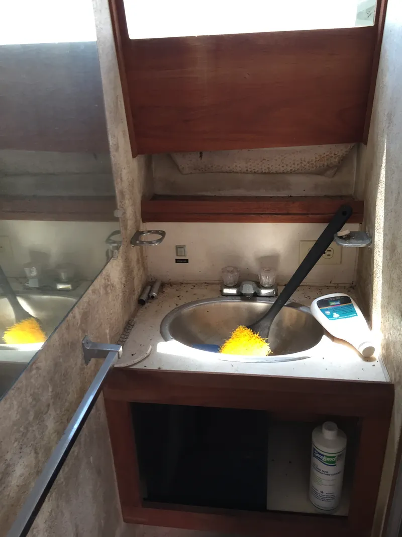 Slide: The Image of 1980 Trojan F-30 Flybridge Sedan bathroom sink with cleaning supplies and mirror. - 9