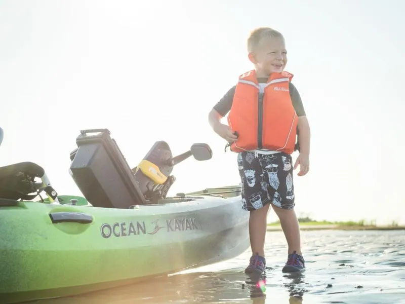 Slide: The Image of Young boy in life vest beside 2023 Ocean Kayak Malibu PDL on a sunny day. - 3