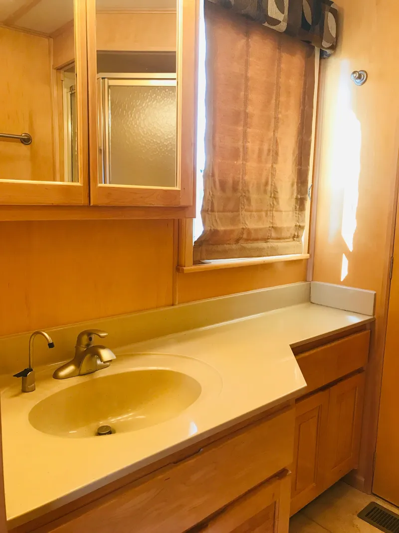 Slide: The Image of 2005 Stardust Cruisers bathroom with wooden cabinets, sink, and window with curtain. - 31