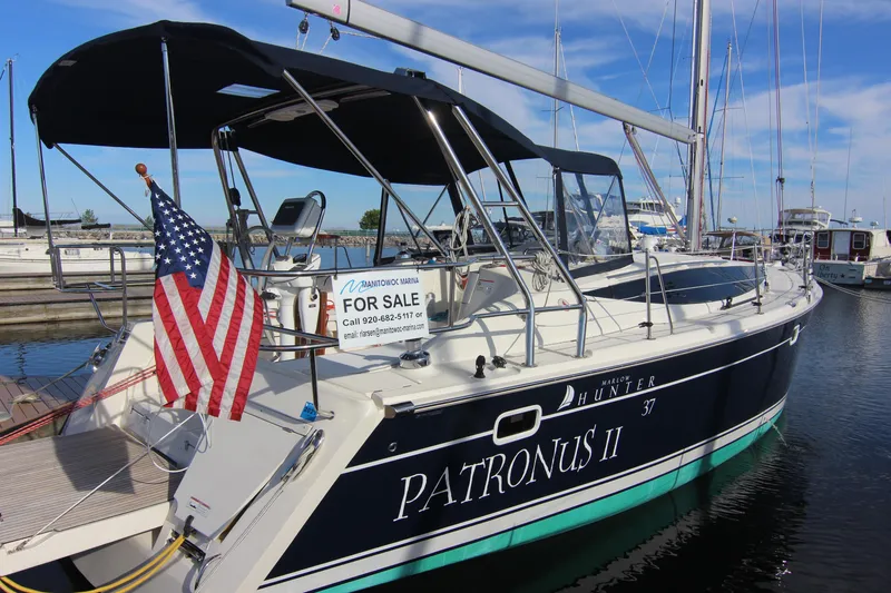Slide: The Image of A 2015 Marlow-Hunter 37 sailboat docked in a marina. It features a blue hull design and an American flag at the stern. - 1