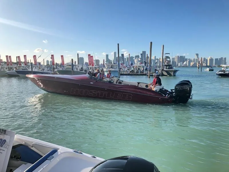 The Image of 2025 Hustler 39 Shotgun boat cruising in a marina with city skyline in the background. - 0