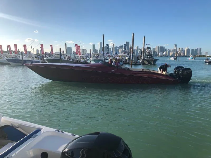 Slide: The Image of Hustler 39 Shotgun 2025 speedboat on water at a marina with city skyline. - 2