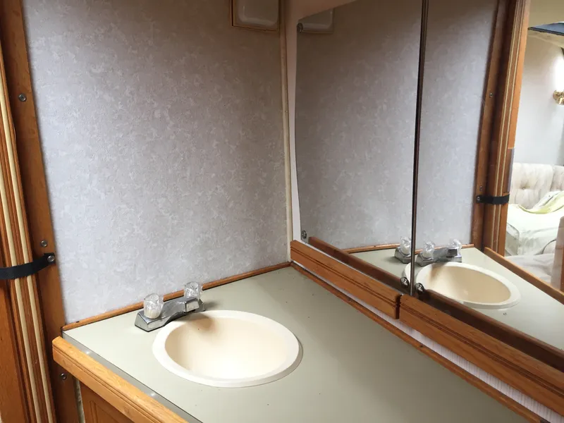 Slide: The Image of 1981 Bayliner 3250 Conquest Sunbridge bathroom with sink, mirror, and wooden accents. - 13