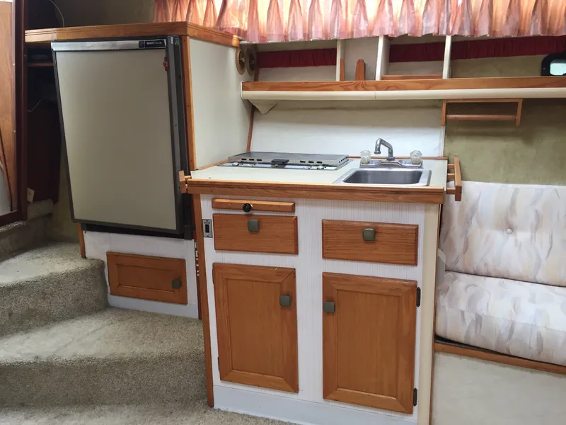 Slide: The Image of 1981 Bayliner 3250 Conquest Sunbridge interior with kitchenette, featuring stove, sink, and fridge. - 9