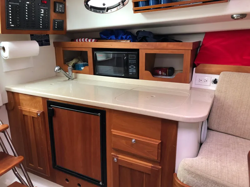 Slide: The Image of 2008 Back Cove 29 boat interior with kitchenette, featuring sink, microwave, and wooden cabinetry. - 18
