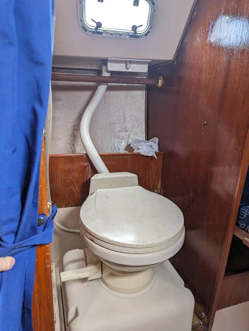 Slide: The Image of 1987 Catalina 25 sailboat bathroom with marine toilet and wooden paneling. - 19