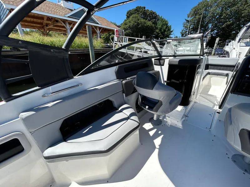 Slide: The Image of 2019 Rinker Q5 OB boat interior with seating and helm, docked under clear blue sky. - 16