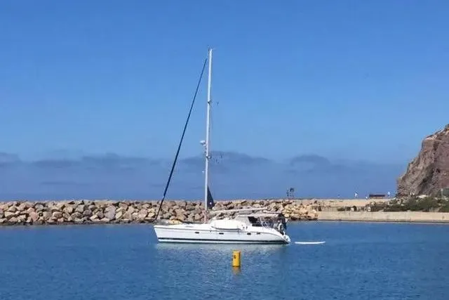 Slide: The Image of Sailboat Hunter 460 (2000) in a calm harbor with rocky breakwater and clear blue sky. - 71